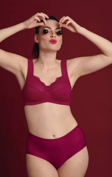 Frau in bordeauxroter Unterwäsche posiert mit Sonnenbrille vor rotem Hintergrund.